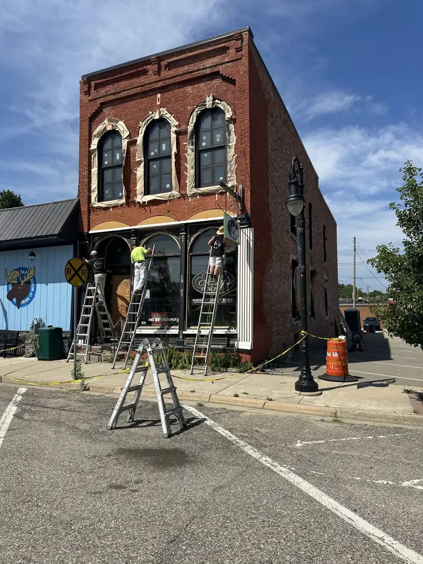 Crews on ladders finishing the restored brick storefront of Andy's Place