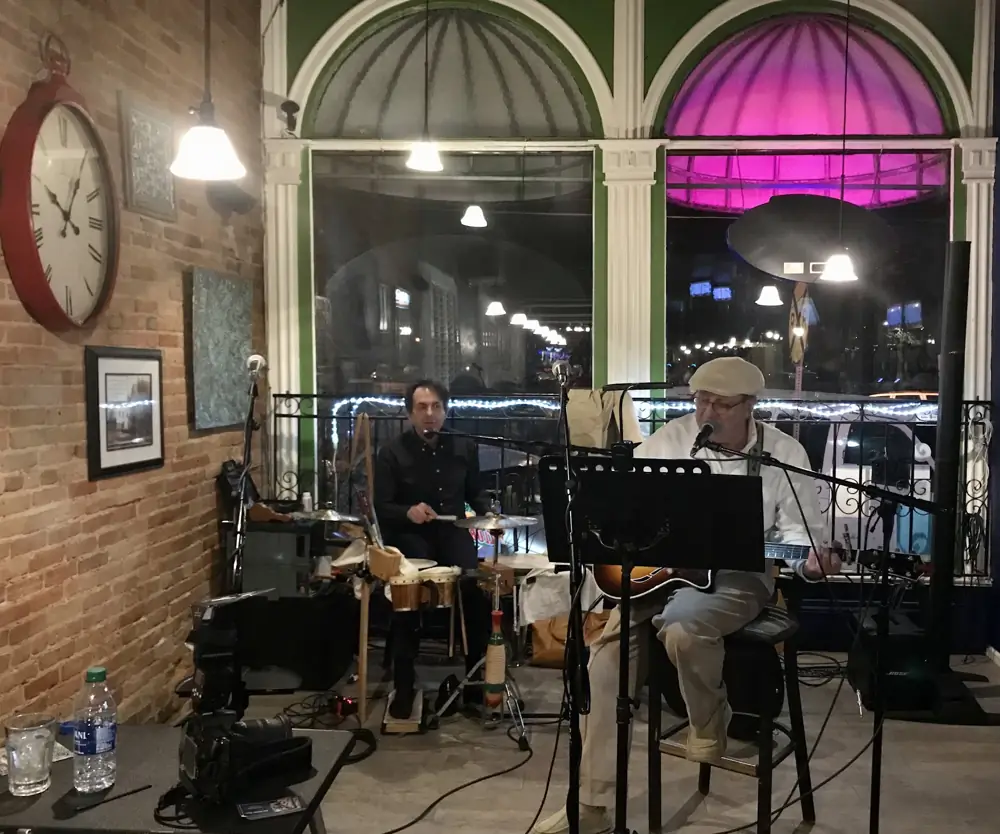 Two musicians playing in front of Andy's arched front windows