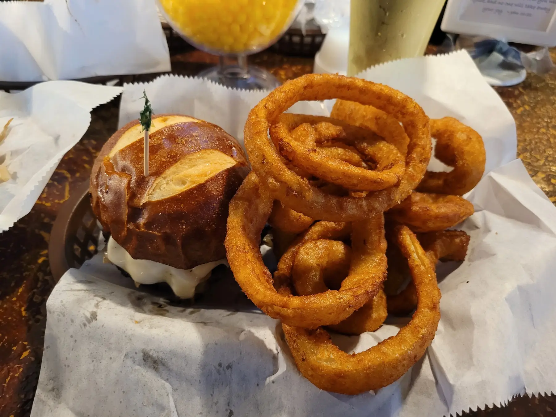 A burger on a pretzel bun next to a tall pile of golden onion rings